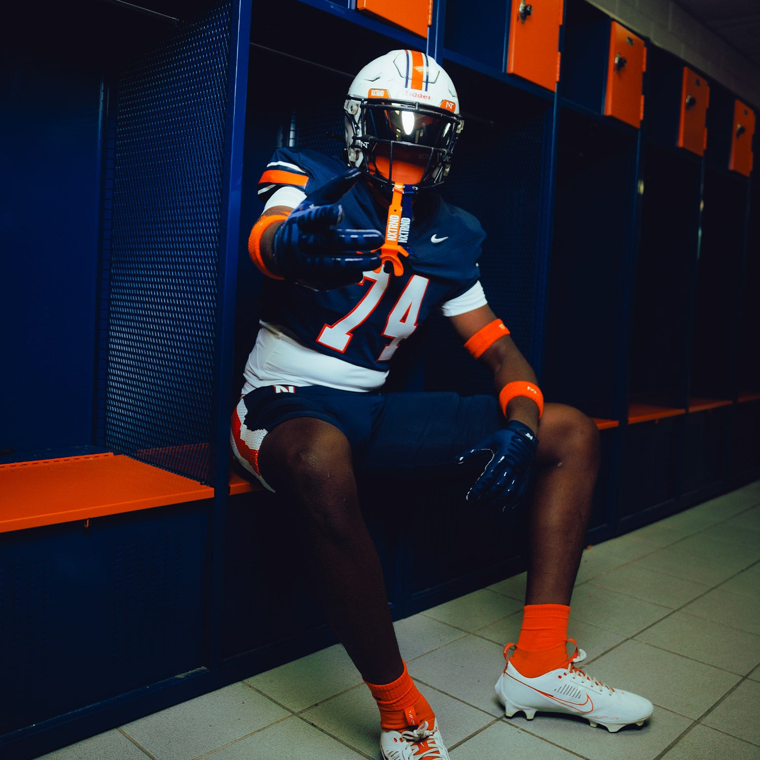 High School Football Player in Locker Room Wearing NXTRND Wrist Band Orange and Double TWO Football Mouthguard